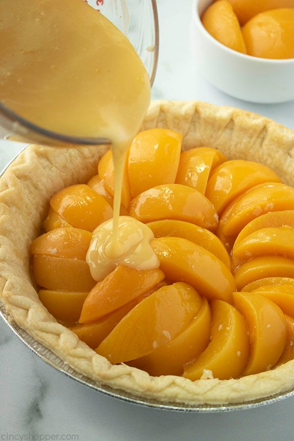 a pie crust filled with sliced peaches being drizzled with orange juice