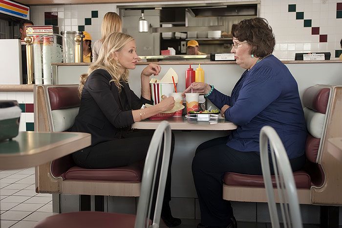 two women sitting at a table in a restaurant talking to each other and eating food