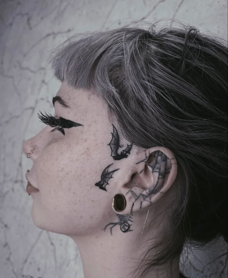 a woman with black tattoos on her face and behind her ear is looking at the sky