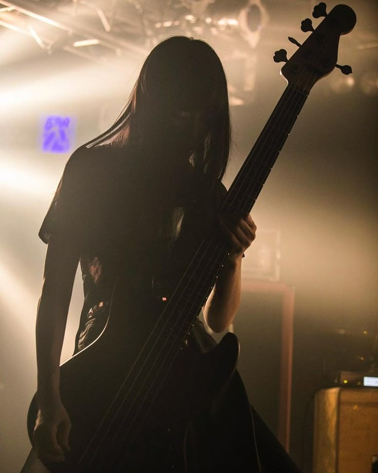 a woman with long hair holding a bass in front of a microphone and stage lights