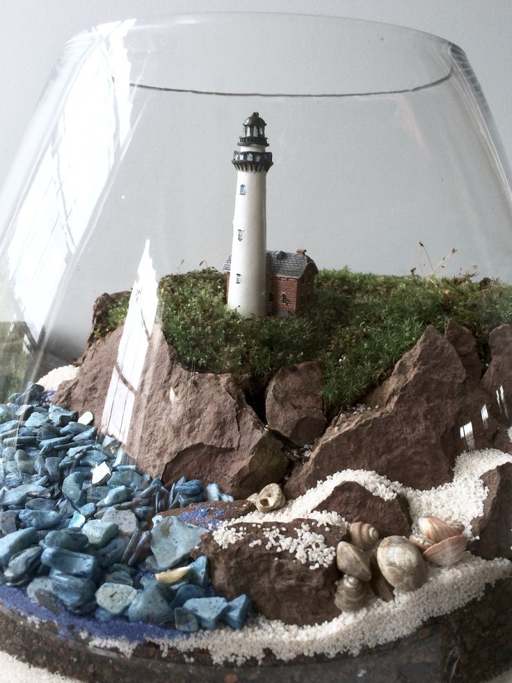 there is a glass bowl with rocks and a lighthouse in it on the counter top