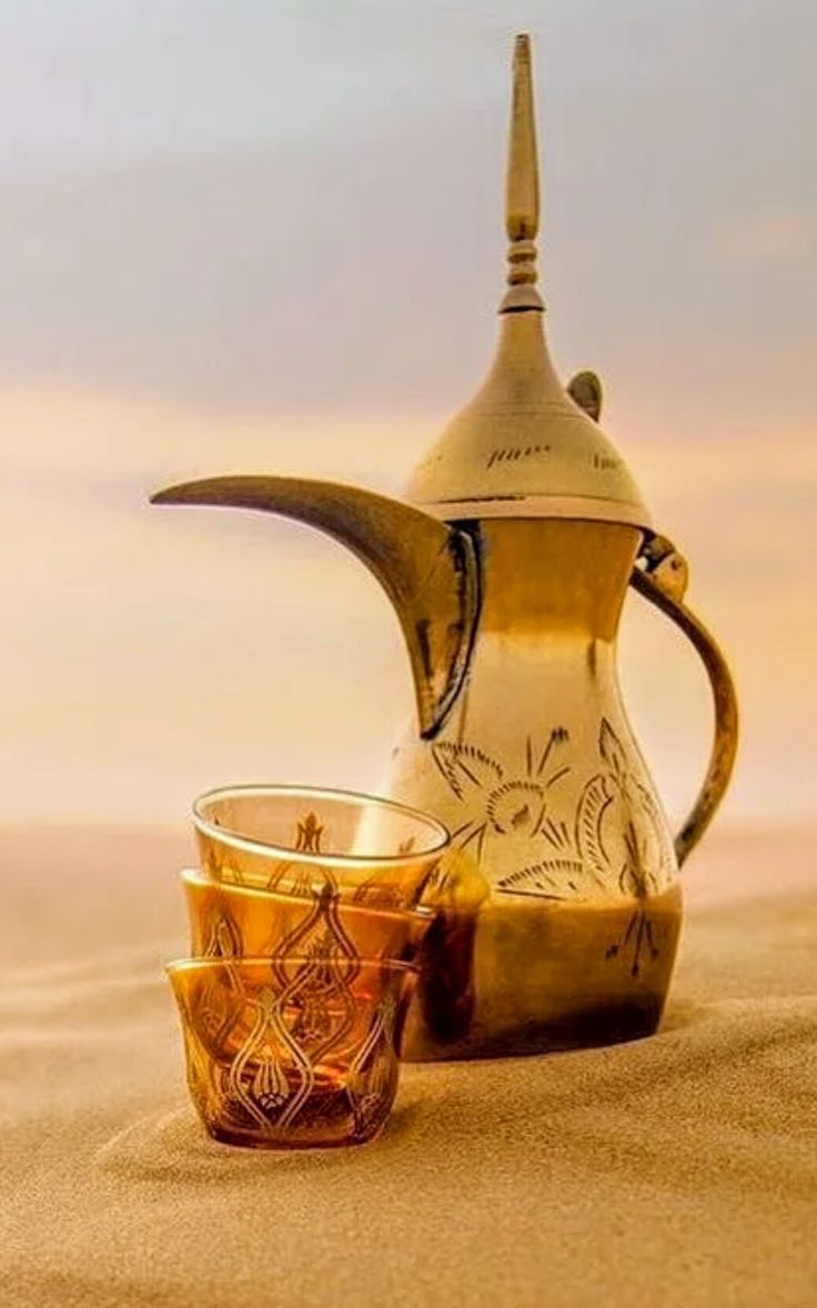 a tea pot and two cups sitting in the sand with an artistic design on it