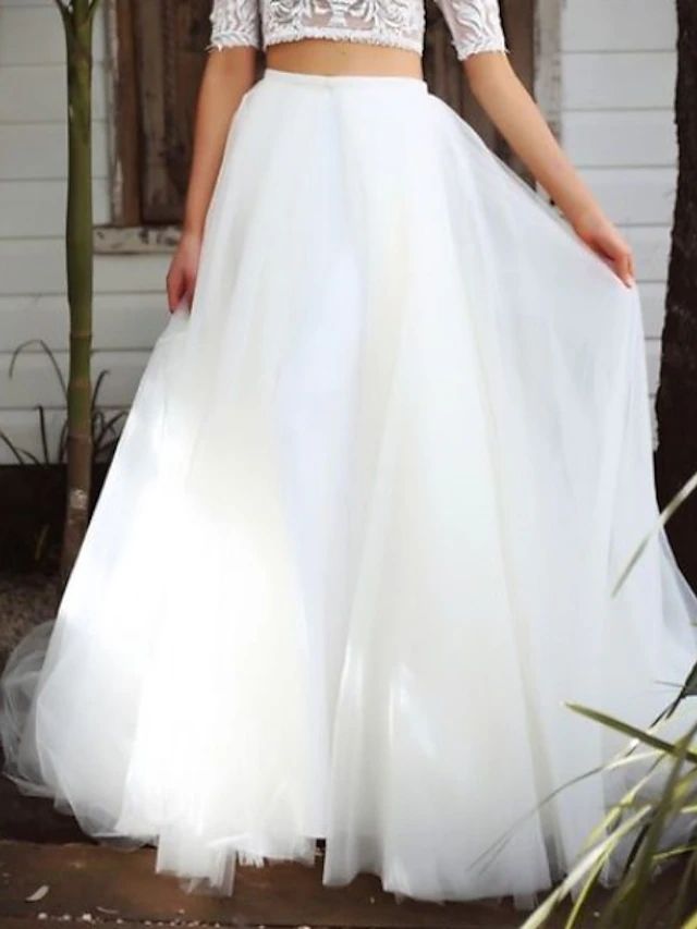 a woman standing in front of a tree wearing a white skirt and cropped top