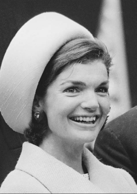 a black and white photo of a woman wearing a hat smiling at the camera with another person in the background