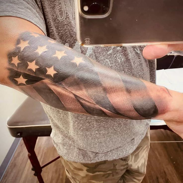 a man is taking a selfie with his cell phone while wearing an american flag sleeve tattoo