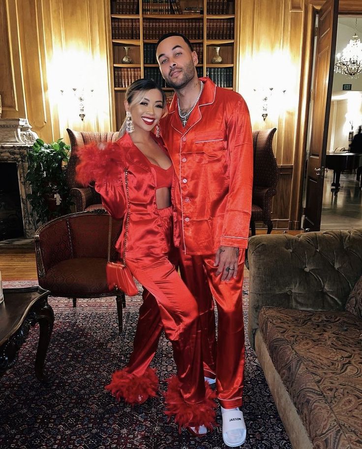 a man and woman in matching red pajamas posing for a photo with a fireplace behind them