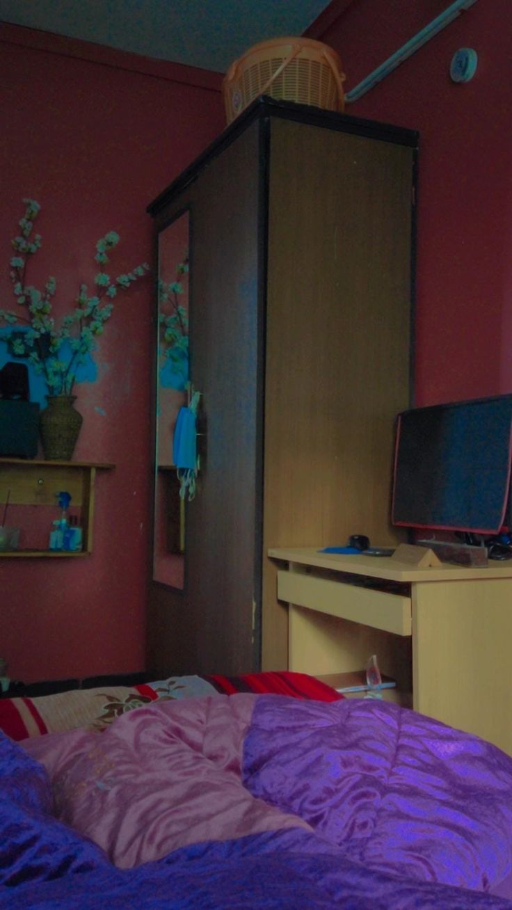 a bedroom with pink walls and purple comforter on the bed in front of a computer desk