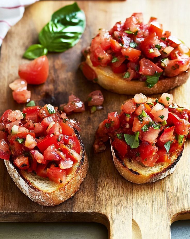 three pieces of bread with tomatoes and basil on them sitting on a wooden cutting board