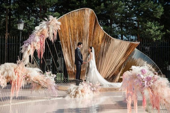 a bride and groom standing in front of a large sculpture with pink feathers on it