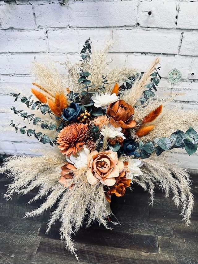 a vase filled with lots of flowers on top of a wooden floor next to a brick wall