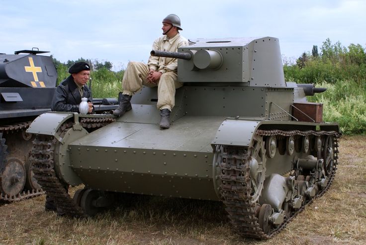 two men sitting on top of a tank in a field next to another one with a cross on it