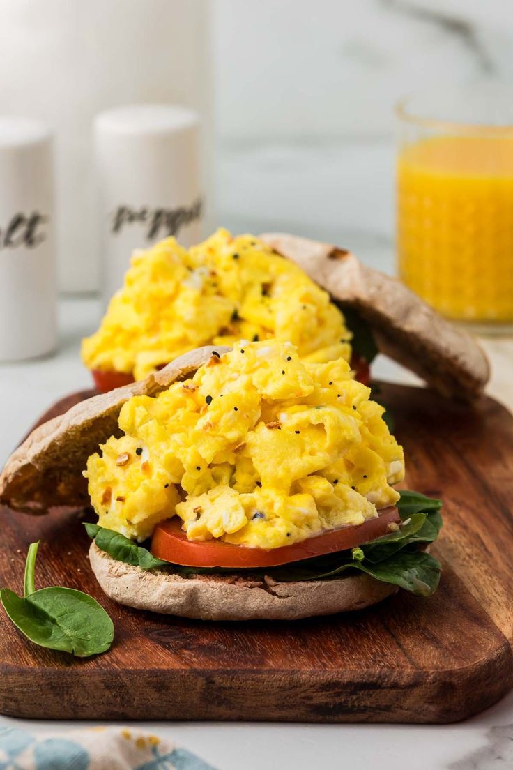 an open face sandwich with scrambled eggs and spinach leaves on a wooden cutting board