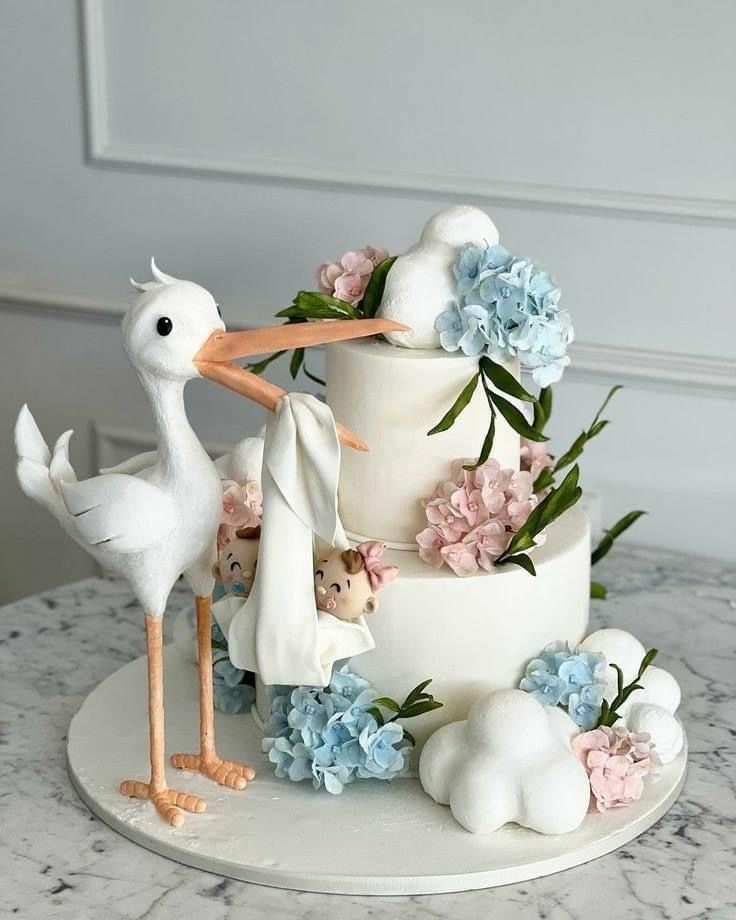 a white cake decorated with blue and pink flowers is topped with a stork figurine