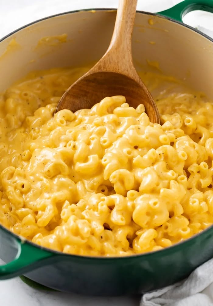 macaroni and cheese is being stirred in a green pot with a wooden spoon