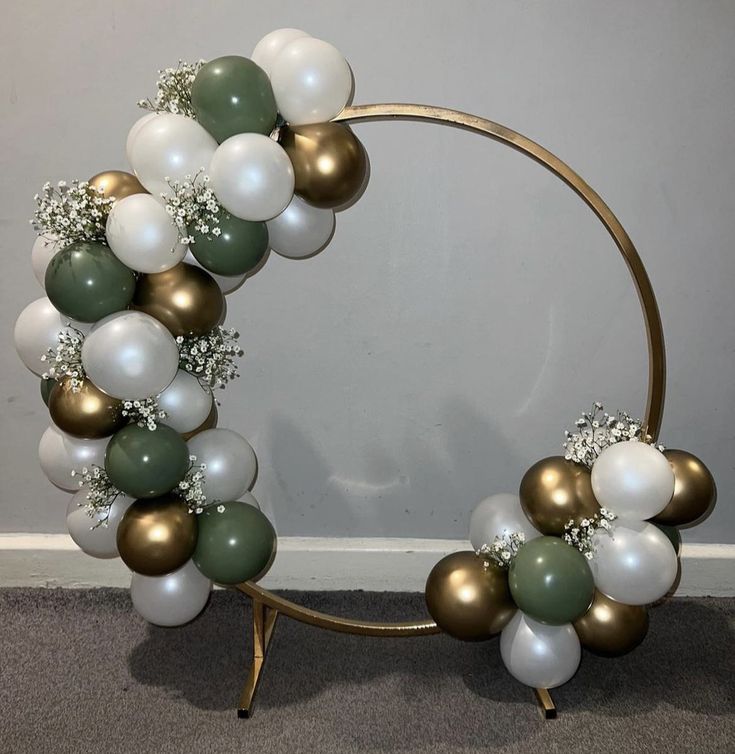 a wreath made out of balloons and greenery on a metal stand in front of a wall