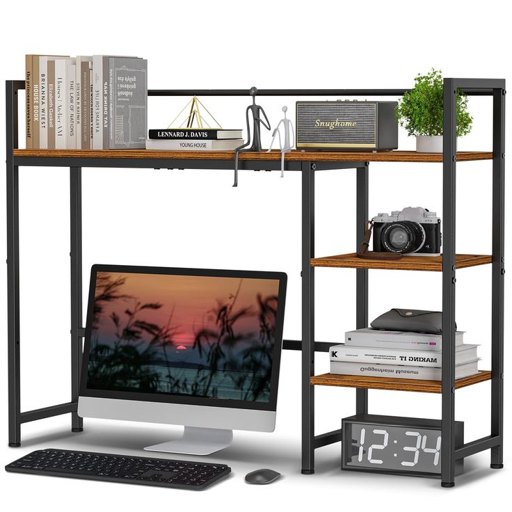 a computer desk with a monitor, keyboard and clock next to books on the shelf