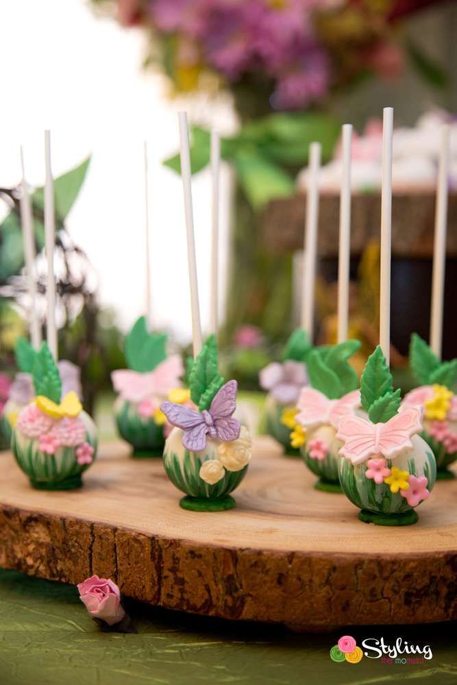 cake pops with flowers and butterflies on them sitting on a wooden board next to candles