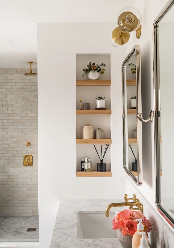 a bathroom with marble counter tops and gold faucet, open shelving above the sink