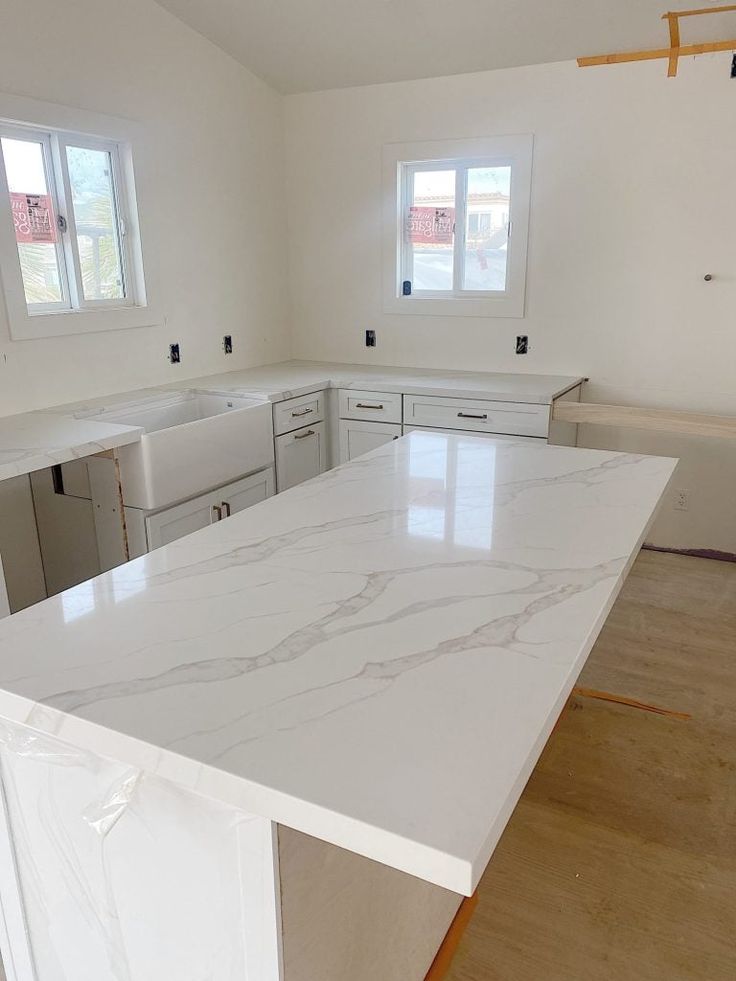 an empty kitchen with white cabinets and marble counter tops