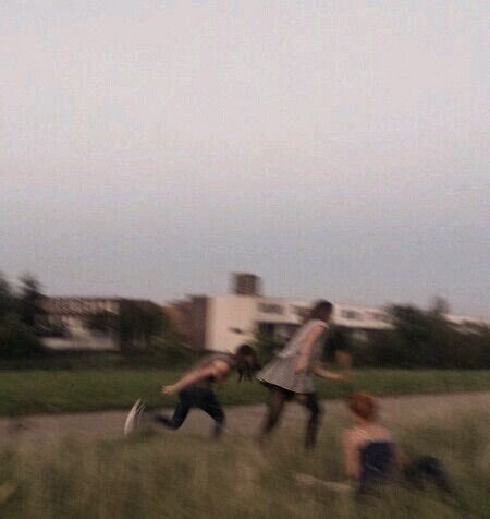 three people are playing frisbee in the grass near a road and buildings at dusk