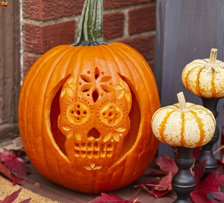 two carved pumpkins sitting next to each other in front of a brick building with leaves on the ground