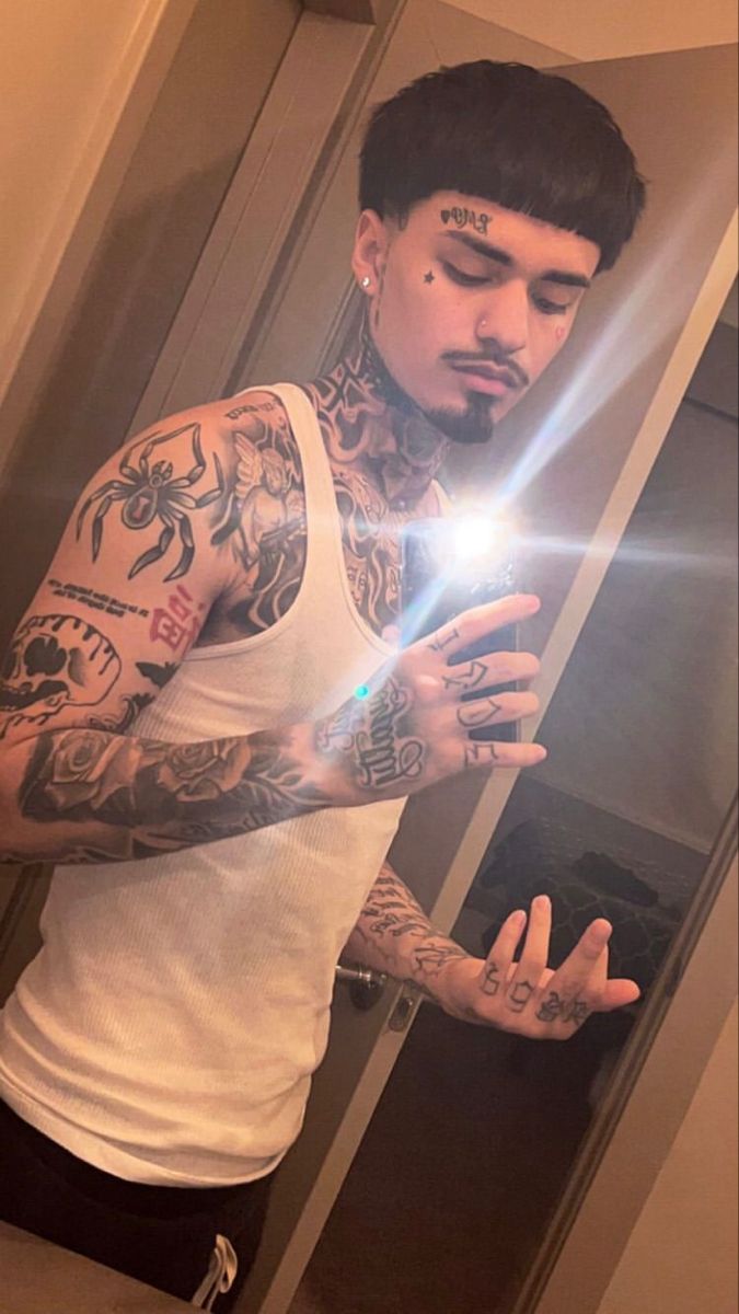 a man with tattoos is looking at his cell phone in the mirror and holding it up