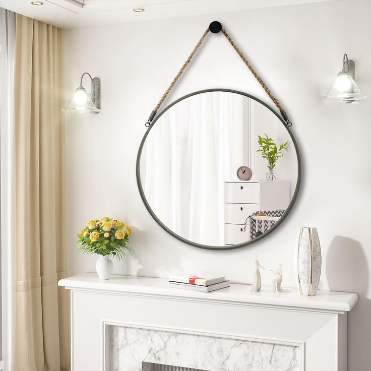 a white fireplace with a round mirror on the mantle and flowers in vases next to it