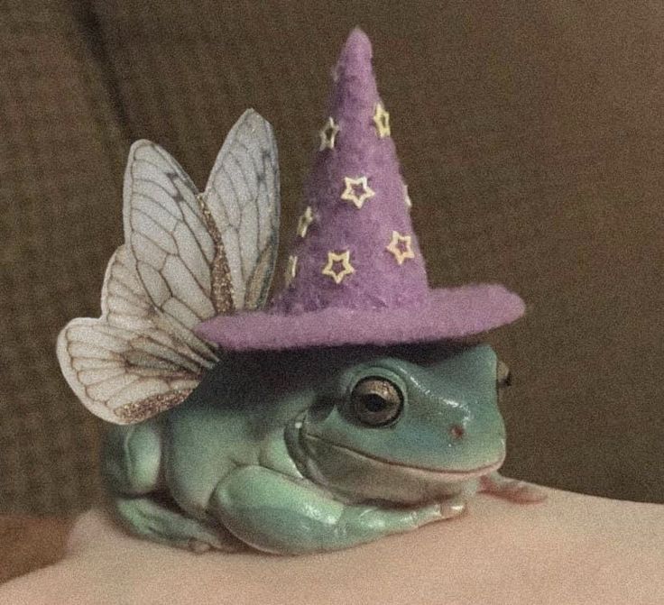 a green frog wearing a purple hat with stars on it's head and wings