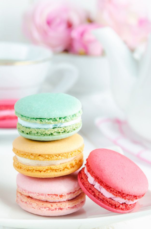 colorful french macaroons on a white plate with pink flowers in the background