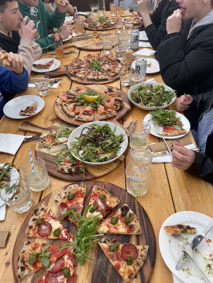 a group of people sitting at a table with pizzas and salads on it