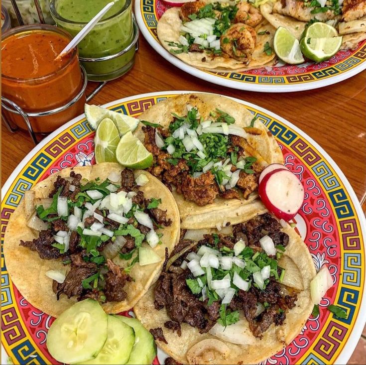 three tacos with meat, onions and cilantro on a colorful plate next to a glass of green juice