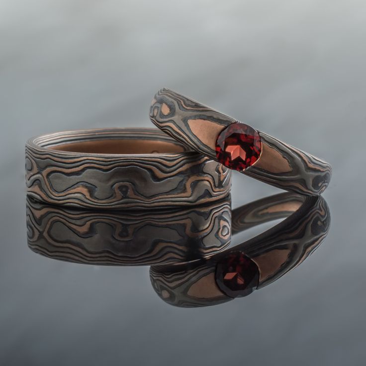 "This custom Mokume Gane Wedding Band Set features our Embers Palette, and Cathedral Set Garnet. We can certainly source similar or different stones for this design. *Price does NOT include stones or setting fees* One band is 6mm in width, and the other is 5-3mm tapered width. They are both shown in our Embers Metal Palette. The Embers Metal Combination features 14k Red Gold, Palladium, and Sterling Silver. They also have an Etched Finish and Flat Profile. Ring 1 - Width: 6mm Pattern: Woodgrain Mokume Gane Ring Wedding, Wedding Ban, Ring Wedding Set, Mokume Gane Ring, Woodgrain Pattern, Twist Pattern, Mokume Gane, Morganite Engagement Ring, Wedding Band Sets