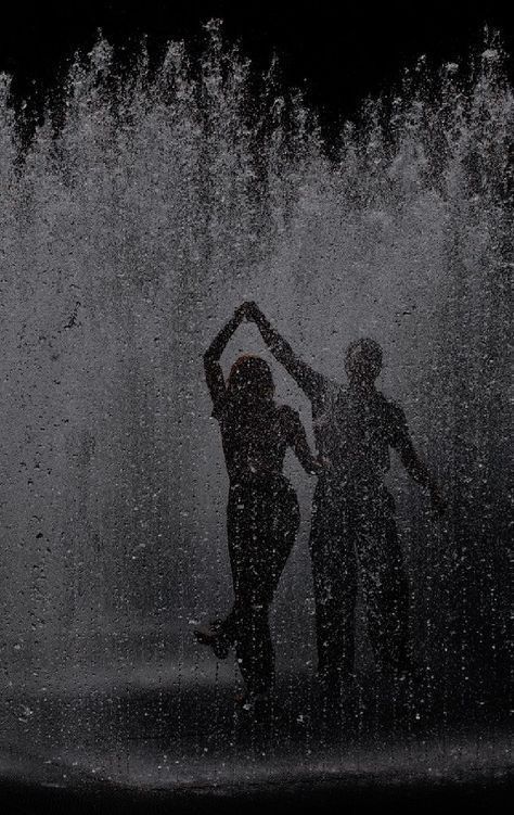 two people standing in front of a fountain with water splashing all around their bodies