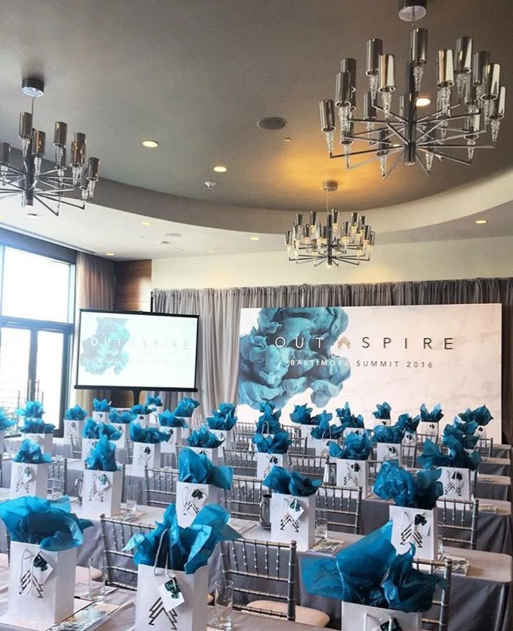 a room filled with lots of tables covered in blue and white chairs next to a projector screen