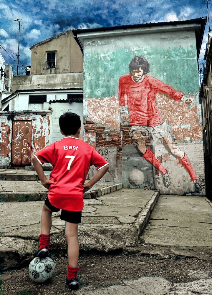 a young boy standing next to a soccer ball in front of a painting on the side of a building