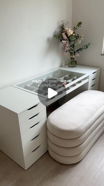 a white desk with drawers and a glass table top in front of a vase filled with flowers