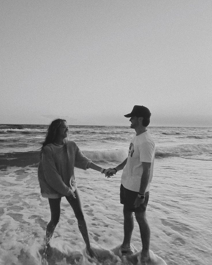 black and white photograph of two people holding hands on the beach with waves coming in