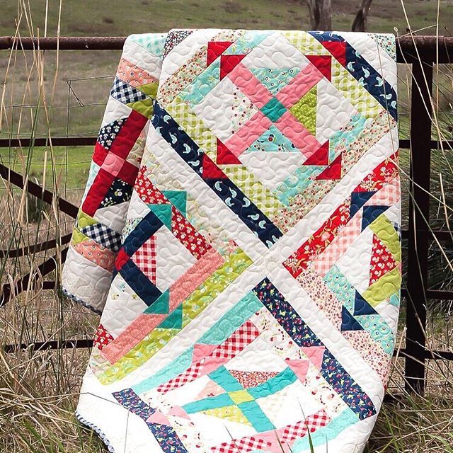 a colorful quilt sitting on top of a wooden fence next to tall grass and trees