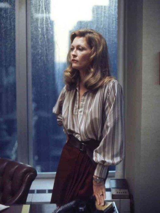 a woman standing in front of a window next to a brown leather chair and desk