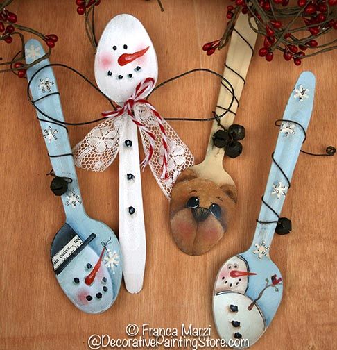 three spoons decorated with snowmen and red berries are sitting on a wooden table