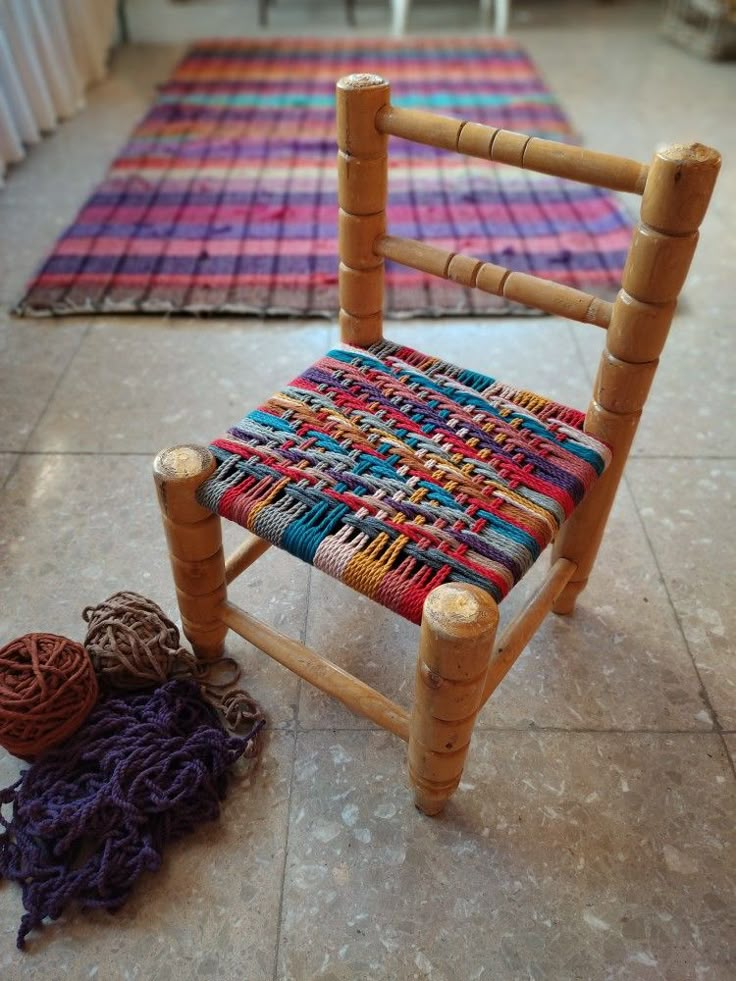 a wooden chair sitting on top of a tile floor next to a pile of yarn