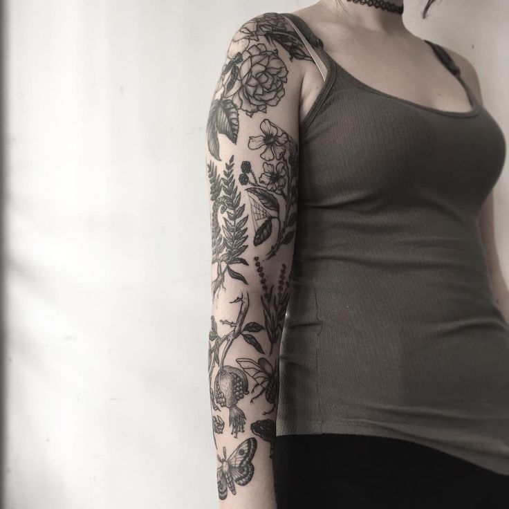 a woman with a tattoo on her arm and shoulder is standing in front of a white wall