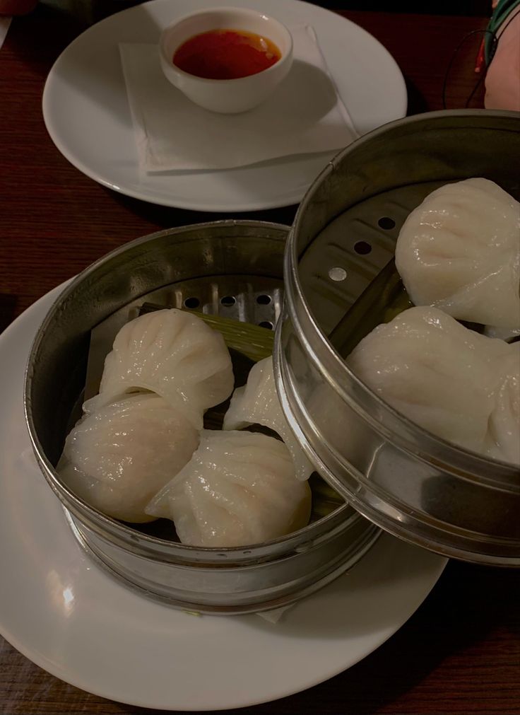 some dumplings are sitting in small metal containers on a plate next to a cup and saucer