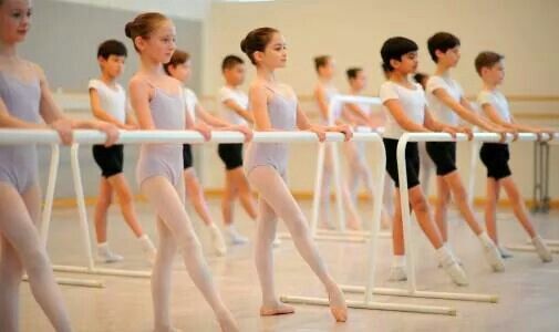 young ballerinas lined up behind the bars in a ballet class