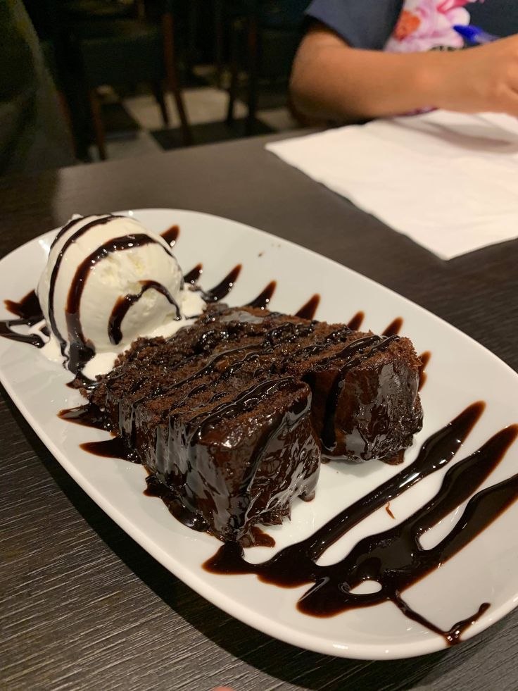 a piece of chocolate cake on a white plate with ice cream and drizzle