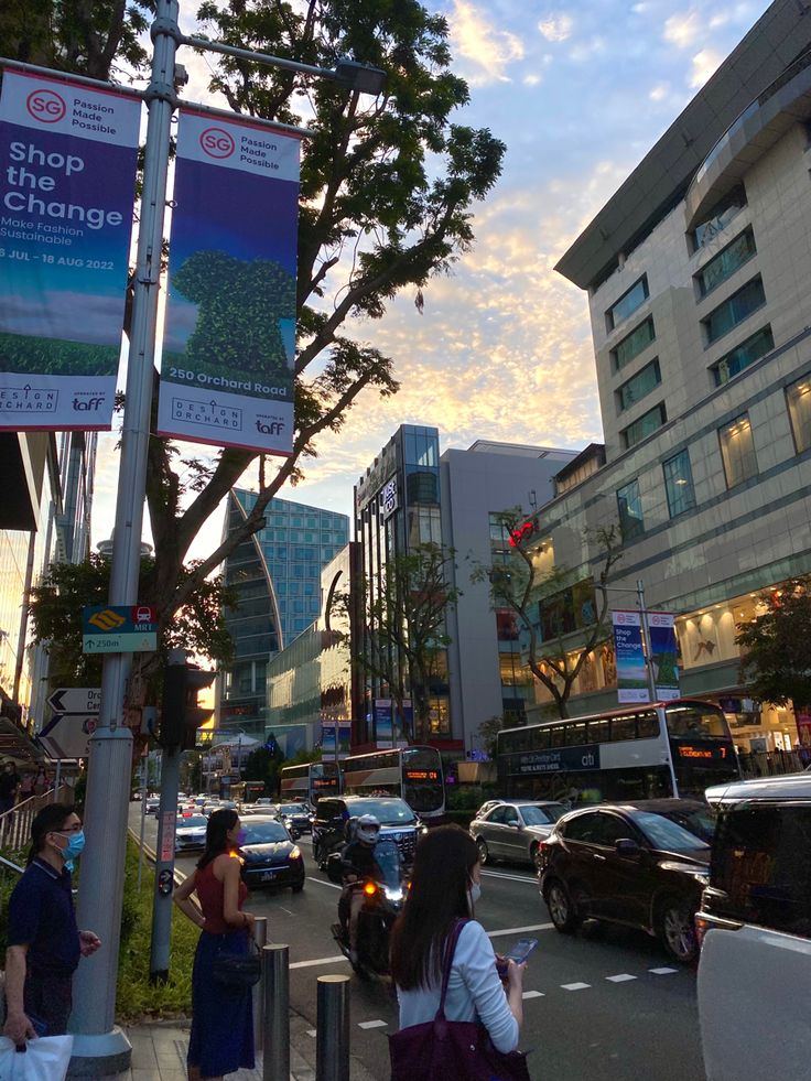 people are walking on the sidewalk in front of some tall buildings and cars parked along the street