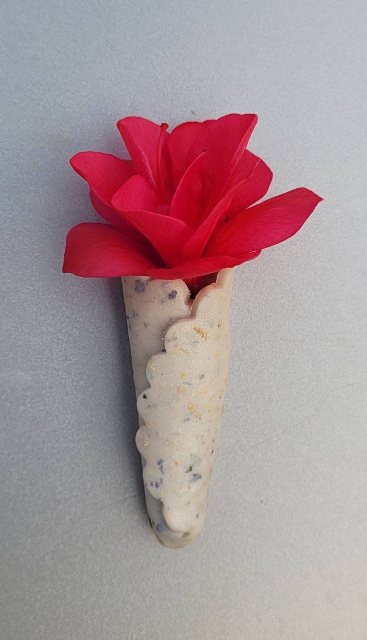 a red flower in a white vase on a table with grey background and gray flooring