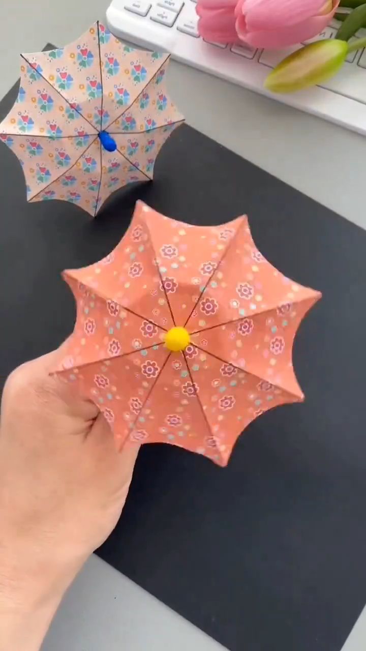 someone is holding an open umbrella next to another opened umbrella on a desk with flowers in the background