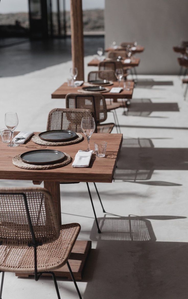 the tables and chairs are lined up on the concrete floored outdoor dining area, with empty wine glasses