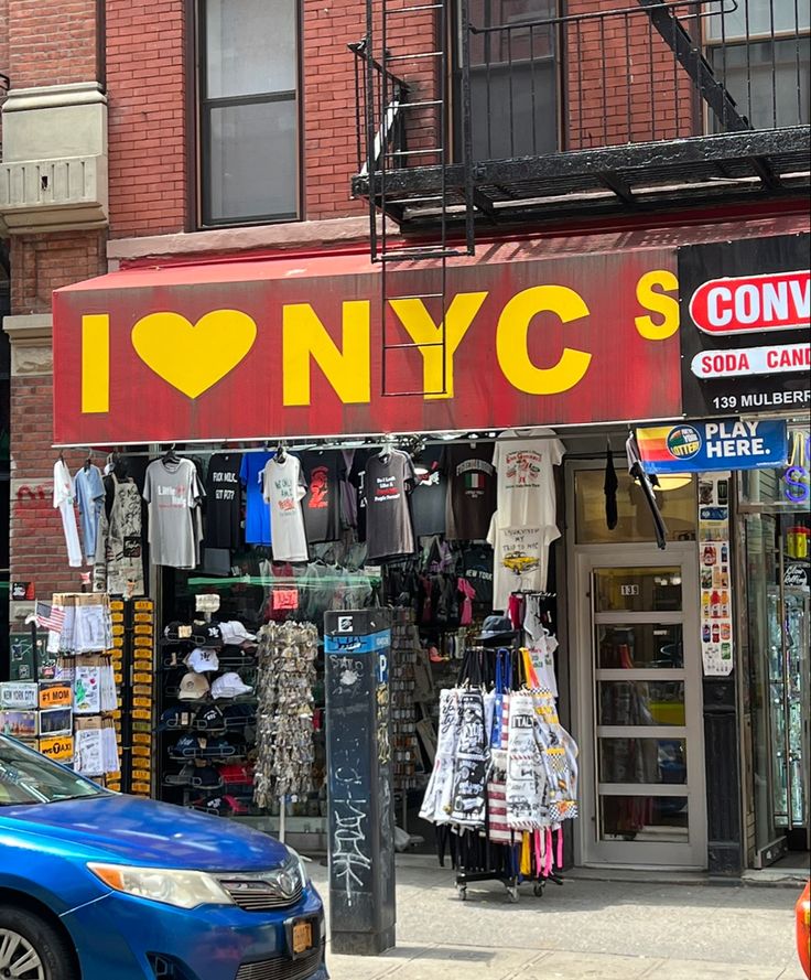 a blue car is parked in front of a clothing store that sells clothes and t - shirts